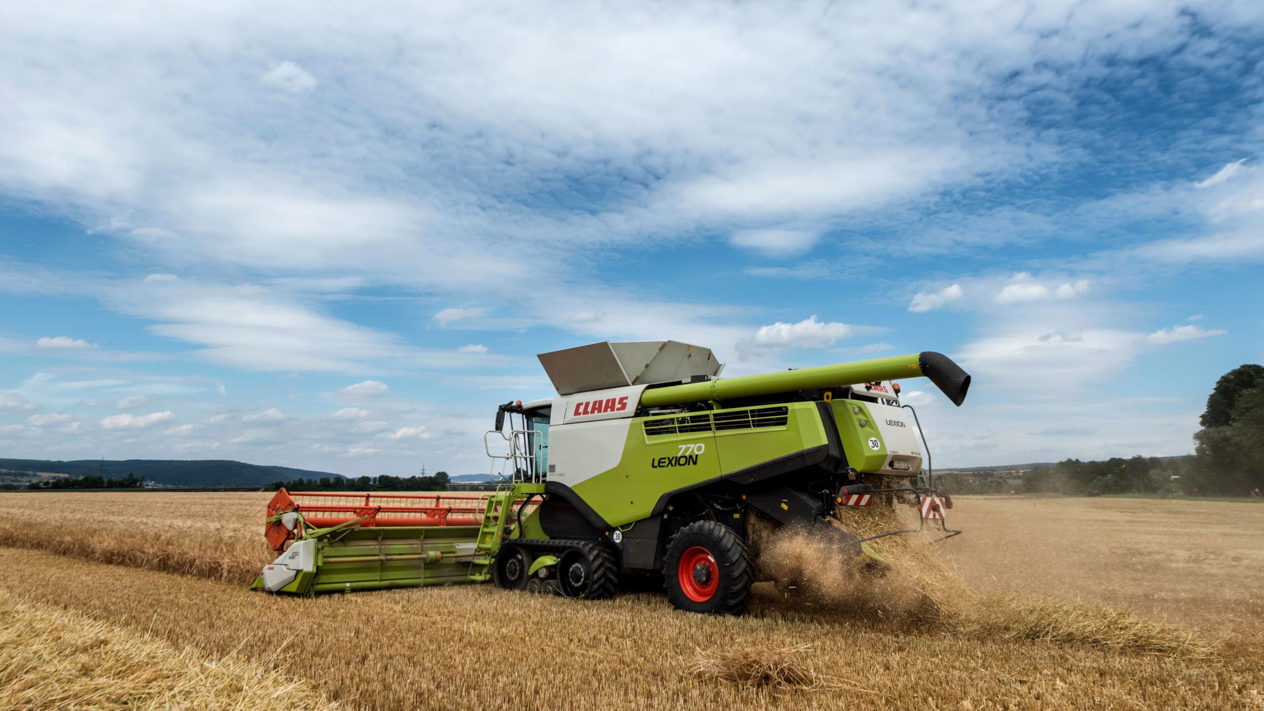Combine harvester harvesting wheat in a rural field under a bright cloudy sky.